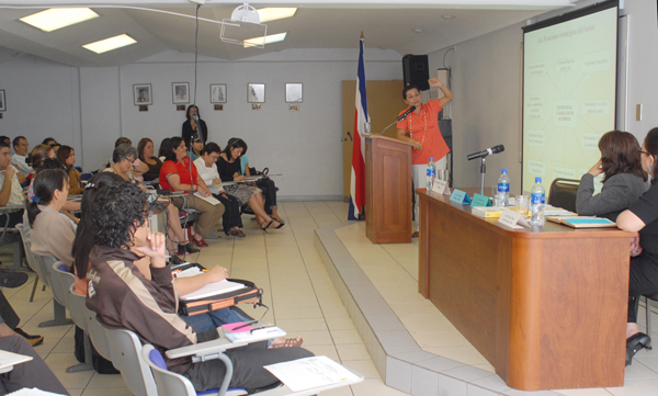 Ana Isabel García presentando, mesa principal y público en auditorio