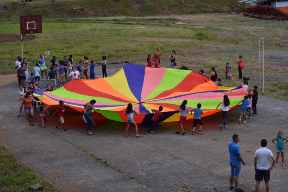 Grupo de personas jóvenes juegan alrededor de una gran manta de colores