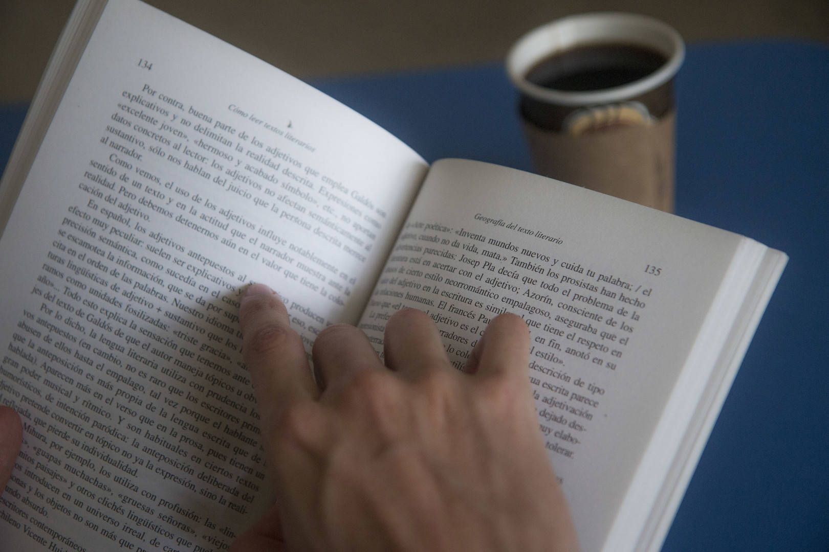 Manos abriendo un libro junto a una taza de café