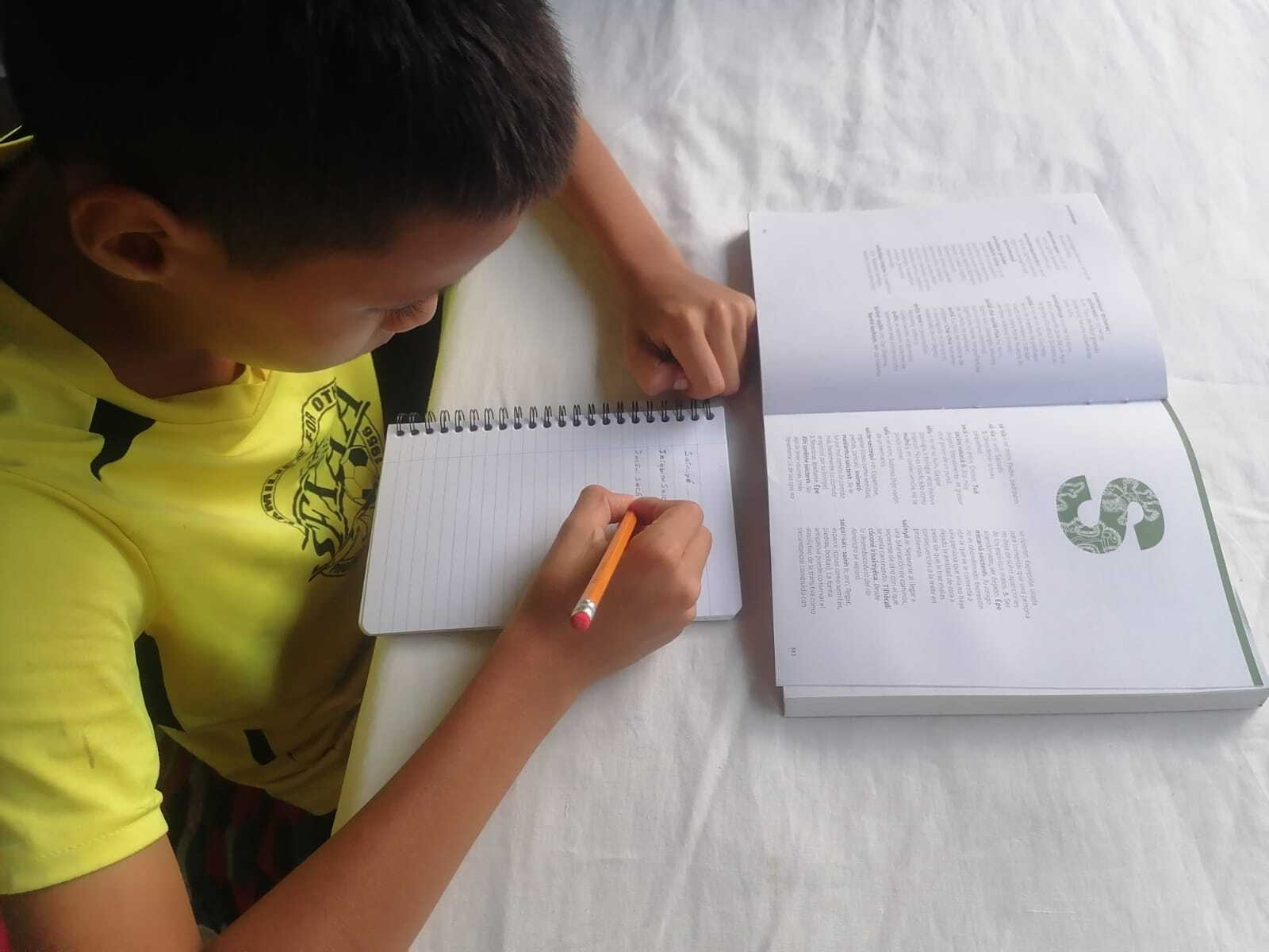 Un niño consulta el diccionario malecu sobre una mesa y toma apuntes de él.
