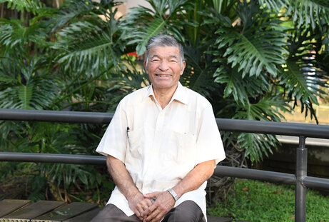 Jorge Enrique Romero Pérez sonriente y sentado en una banca de un jardín de la Sede Universitaria …