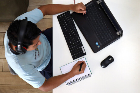 Vista aérea de un joven utilizando una computadora portátil sobre un escritorio y tomando apuntes …