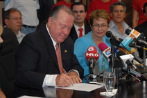 Dr. Luis Paulino Mora firmando. Atrás, la rectora Yamileth González
