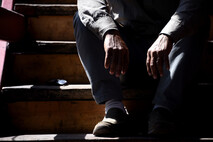 Hombre sentado en unas gradas oscuras sin que se le vea la cabeza. Sus brazos están entre sus …